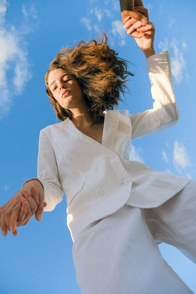 Low angle shot of a stylish woman in white clothes against a blue sky, embodying freedom and elegance.
